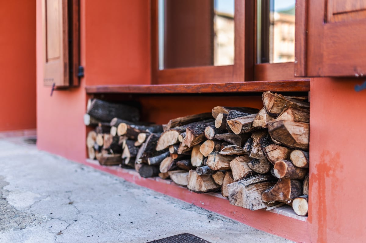 Stacked firewood stored beneath a wooden window in a village house